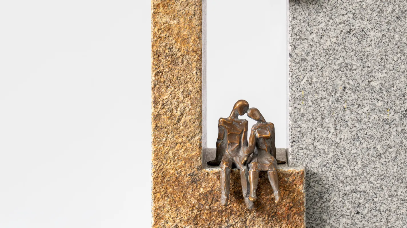 Grabmal mit zwei Bronzefiguren die sich umarmen